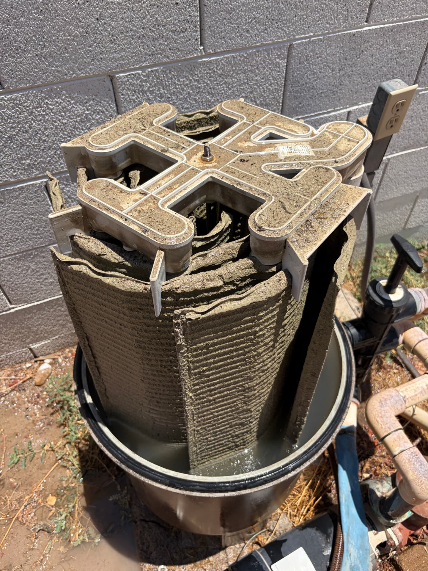 A diatomaceous earth filter grid assembly sitting inside an open filter tank, coated in thick brown sediment
