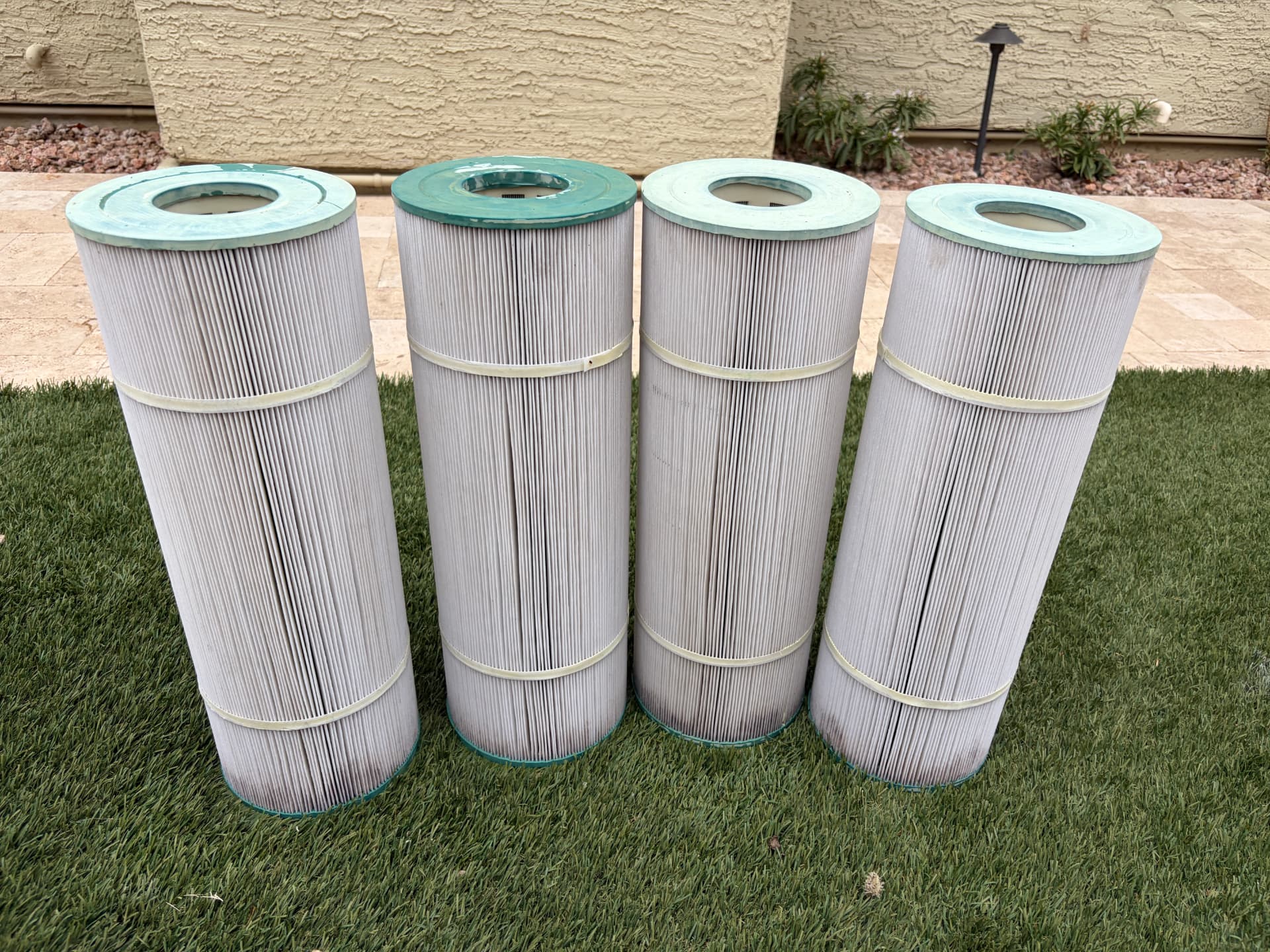The same four pool cartridge filters, clean and white after being washed