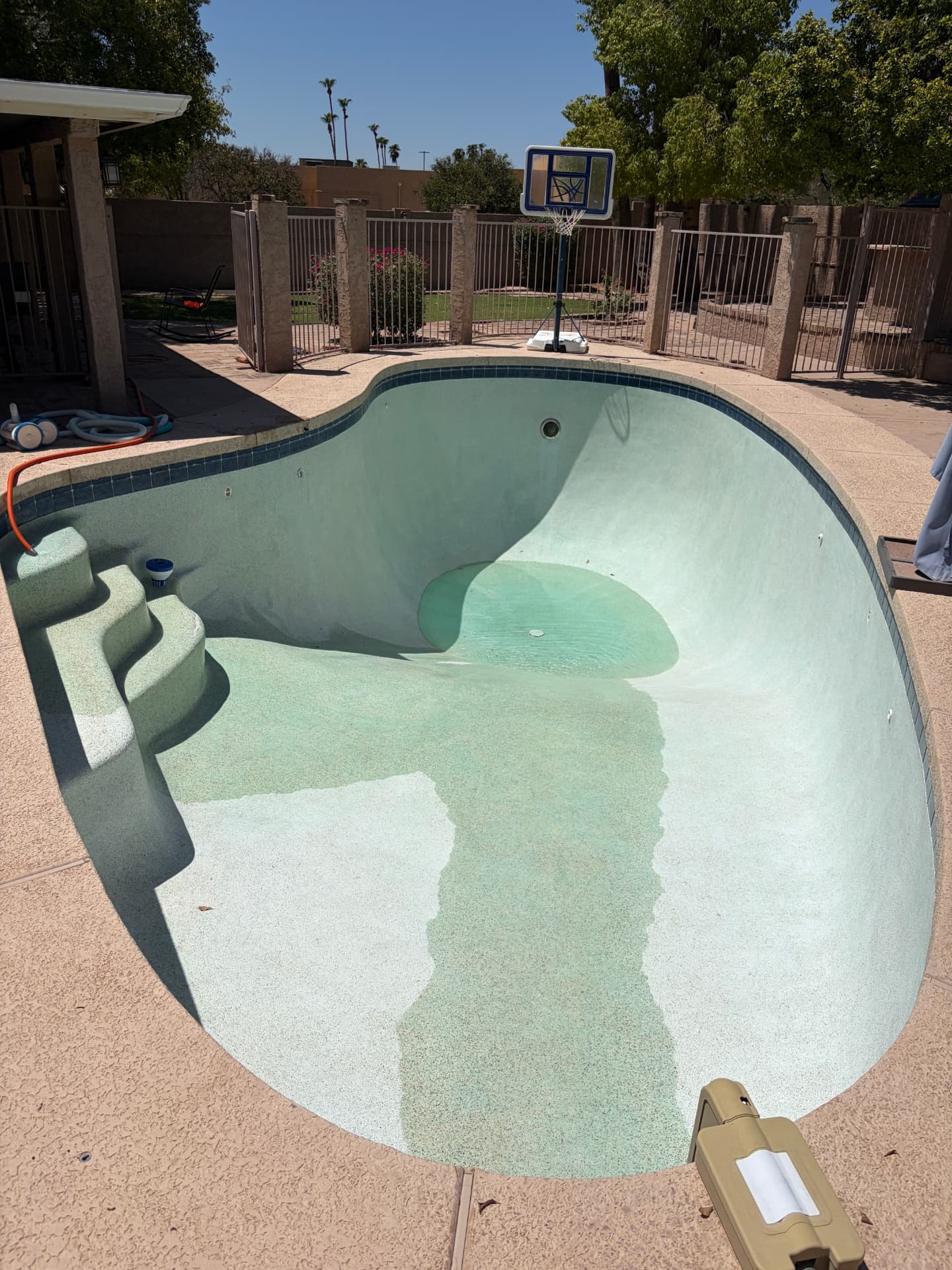 The same pool after pressure washing and rinsing, showing clean plaster and a patch of clear water in the deep end